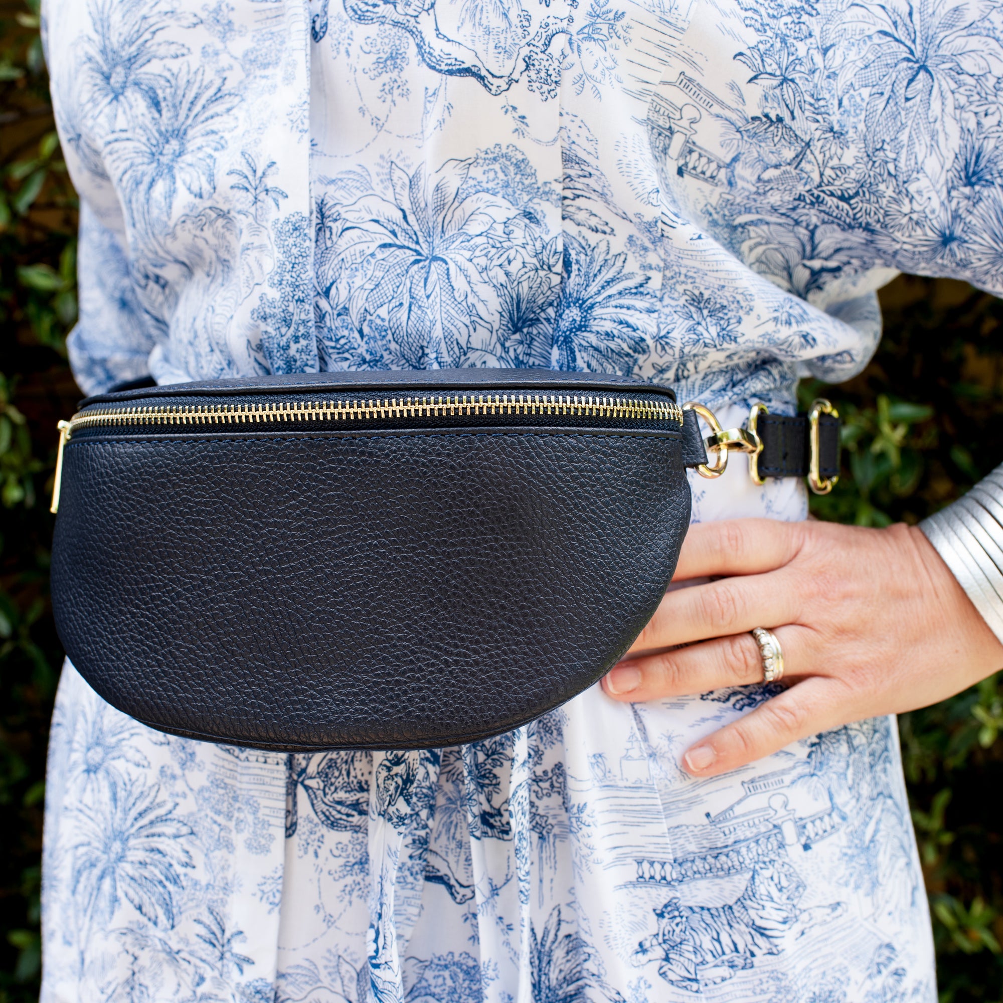 a woman wearing a navy crossbody /waistbag with gold hardware. 
