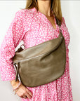 
A woman wearing an XL taupe crossbody bag with silver hardware and an adjustable strap.

